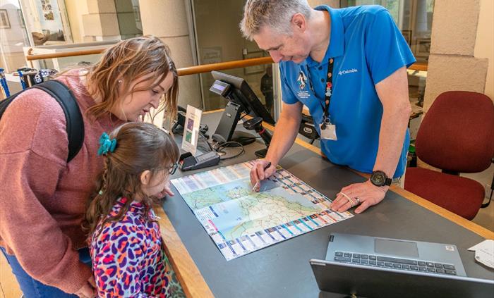 Staff member showing Mother and child Pembrokeshire map at counter to understand the local area.